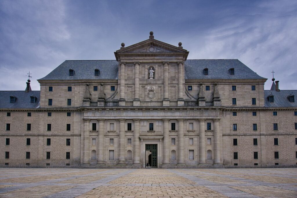 Majestic view of the San Lorenzo de El Escorial Monastery's facade under a cloudy sky.